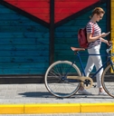 Woman walking her bike along sidewalk, looking down at phone