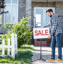 Man putting for sale sign in front of house