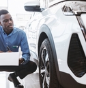 serious auto salesman sitting near new car