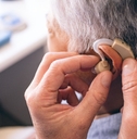 male doctor applying hearing aid to senior woman