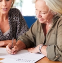 Female Friend Helping Senior Woman To Complete Last Will And Testament At Home