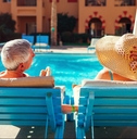 senior couple relaxing by swimming pool lying on chaise-longues