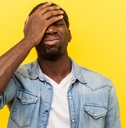 regretful man in denim casual shirt holding hand on face