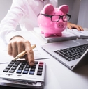 person calculating in front of a piggy bank and a laptop