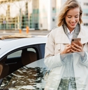 adult woman exiting her car while looking at her phone