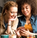 two women smiling and happy while looking at a phone
