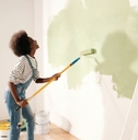 woman dancing and painting wall with roller brush 
