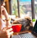 adult woman holding a coffee cup while looking at a stock chart on her laptop