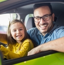 father and daughter smiling behind a driving wheel