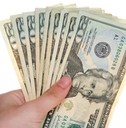 A hand holds several 20-dollar bills arranged in a fan 