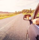 A woman drives down a country road with her arm out the window. 