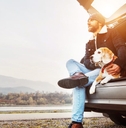 A man and a dog sit on the edge of the cargo area in a hatchback car. 