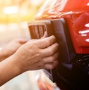 A person putting a license plate holder on the bumper of a red car.