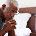 depressed senior man looking unhappy sitting on side of bed