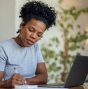 african american woman writing on notepad in front of laptop