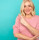happy woman in short hair raising finger at pink backdrop