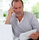 mature man thinking in front of a laptop holding documents