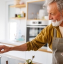 happy senior man cracking eggs and cooking pasta in kitchen