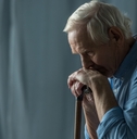 sad senior man leaning on cane in room