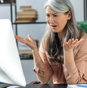 annoyed mature woman looks at computer in confusion
