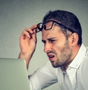 man with glasses squinting eyes at laptop 