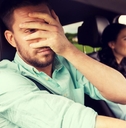 A man in the passenger seat of a car covers his face with his hand. 
