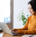 asian woman happily using laptop on table with coffee and files at workspace