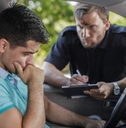 man sitting in car stressing as the police interviews him and write something on the clipboard