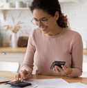 female works with financial papers at home counting on calculator