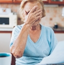 senior woman covering her face in stress while looking at utility bills in kitchen