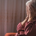 senior lady in depression sitting on couch at home covering her face with hands