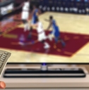 Hand holding a remote in front of a TV playing basketball