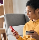 woman wearing yellow hoodie sitting on floor holding card to make payment using smartphone