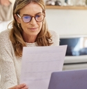 woman sitting at counter top in kitchen reviewing documents while using computer at home