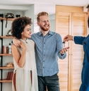 young male real estate agent standing standing inside house handing keys to couple