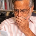 senior man looking at utility bills and covering face in terror