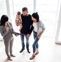 female real estate agent holding papers on clipboard showing new house to couple with baby