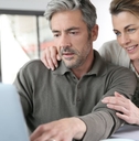 attractive senior couple reviewing financial budget using laptop with papers and cup on table