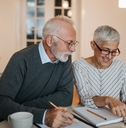 senior couple sitting at wooden table with papers and calculator sorting finances at home for vacation