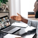 happy african american man sitting on work desk at office using laptop to have virtual video conference with colleagues