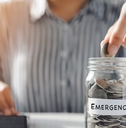 woman putting pennies in glass jar with emergency label on it while using calculator to finance mortgage bills