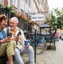 happy senior couple on vacation sitting on stairs of cafe holding cup of coffee 