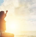 woman on road trip sitting on car bonnet at beachside raising hands in the air