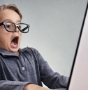 cute boy wearing fake glasses shocked and surprised while using laptop