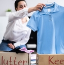 Woman sorting wardrobe into brown boxes with &quot;declutter&quot; and &quot;keep&quot; labels.