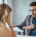 businessman holding papers arguing with young business woman at office