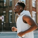 african american man wearing wireless headphones running in street during day time