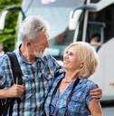 happy senior couple hugging each other on road with tourist bus in background