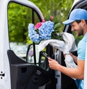 A smiling flower courier gets out of a van holding a bouquet of blue and pink flowers. 