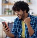 A man looks happy and pumps his fist while looking at his phone. 